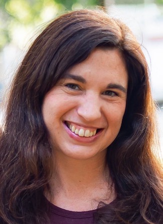 Photo of Rachel Fyall in front of a green background wearing a purple shirt. 